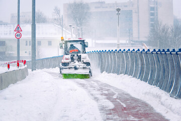 Tractor removing snow with rotating brush and snow plow from pedestrian zone on bridge, sidewalk...