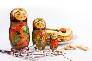 Background with pancakes, wooden dolls matryoshka, sushki and spoon with red caviar on white for Maslenitsa festival.