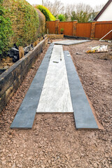Path of porcelain slabs in contrasting colours being laid in the garden of a residential property. No people.