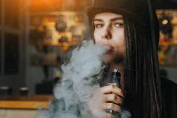 Young pretty woman in cap smoke an electronic cigarette at the vape shop. Hip-hop style. Closeup. - 480805389