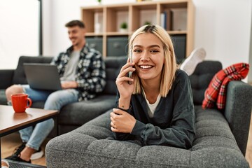 Young caucasian couple smiling happy using laptop and talking on the smartphone at home.