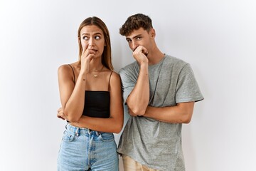 Young beautiful couple standing together over isolated background looking stressed and nervous with hands on mouth biting nails. anxiety problem.