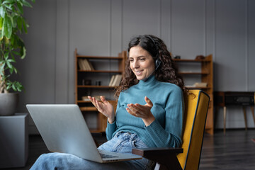 Positive smiling female home office employee wearing headset having video call web conference with...