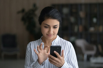 Happy young Indian ethnicity woman using cellphone, typing message, web surfing information, communicating distantly in social networks or shopping in internet store, modern tech addiction.