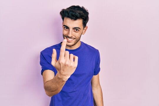 Young hispanic man wearing casual t shirt beckoning come here gesture with hand inviting welcoming happy and smiling