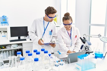 Man and woman wearing scientist uniform using laptop working at laboratory