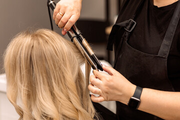 The hairdresser curls the hair of the client with a hair straightener