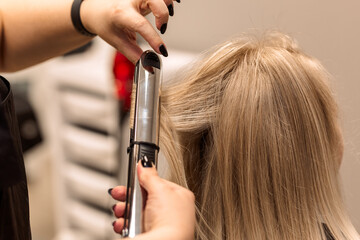 The hairdresser curls the hair of the client with a hair straightener