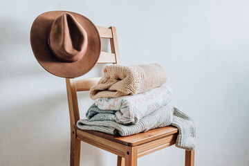 Stack of cozy winter sweaters and hat on the chair on a white background