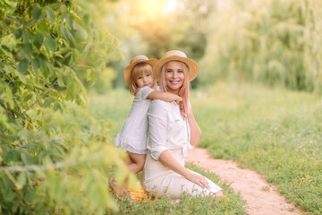 Fototapeta premium Mom and daughter in white clothes and straw hats on a picnic in summer or spring on a sunny day