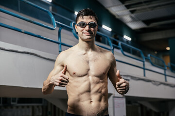 Fototapeta na wymiar Muscular swimmer gives thumbs up in indoor pool