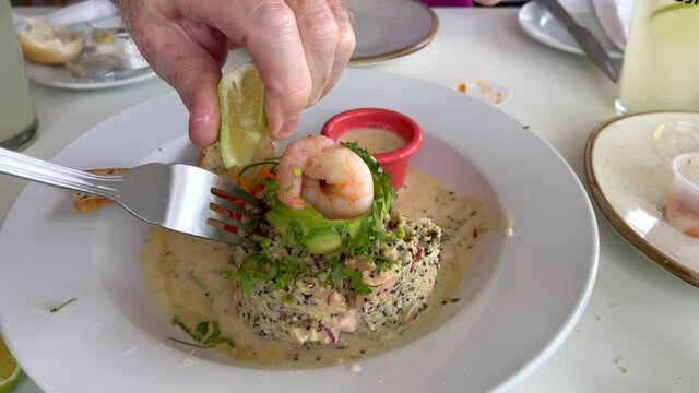 Hand squeezing lemon on salmon quinoa ceviche with avocado and prawns on top. Mixing of traditional gourmet food from Peru