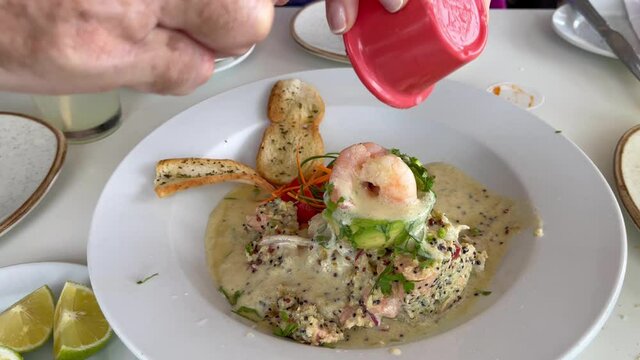 Hand pouring tiger milk on salmon quinoa ceviche with avocado and prawns on top. Mixing of traditional gourmet food from Peru