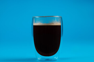Americano coffee on blue background. Espresso in double glass cup.