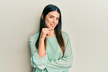 Fototapeta premium Young hispanic woman wearing casual clothes smiling looking confident at the camera with crossed arms and hand on chin. thinking positive.