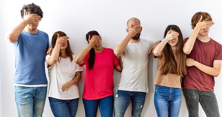 Group of young friends standing together over isolated background covering eyes with hand, looking serious and sad. sightless, hiding and rejection concept
