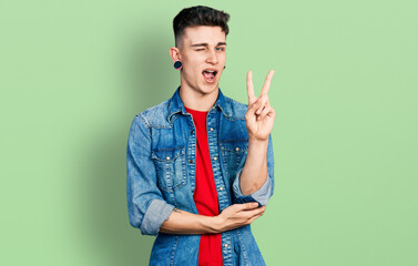 Young caucasian boy with ears dilation wearing casual denim jacket smiling with happy face winking...