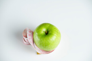 a whole green apple on a white background with a meter (measuring tape)