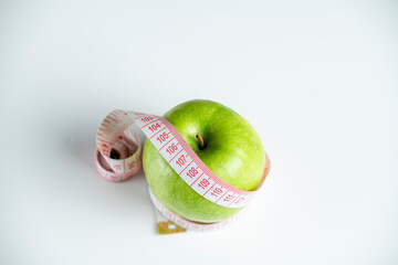 a whole green apple on a white background with a meter (measuring tape)