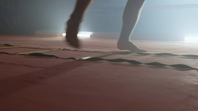 Boxer running on divided sections on floor. Close-up of legs. Barefoot fighter training in dark gym while stepping. 4K, UHD