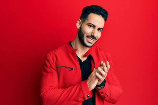 Young hispanic man wearing red leather jacket clapping and applauding happy and joyful, smiling proud hands together