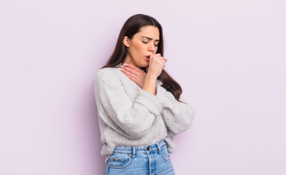 pretty young woman feeling ill with a sore throat and flu symptoms, coughing with mouth covered