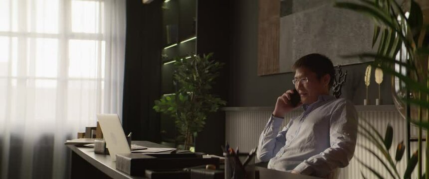 MED Portrait of 40s Asian businessman talking on the phone in his office. Shot with 2x anamorphic lens