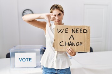 Young blonde woman at political election holding we need a change banner with angry face, negative sign showing dislike with thumbs down, rejection concept