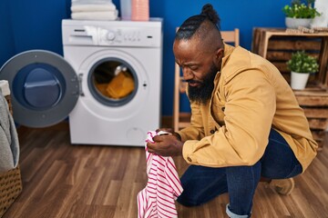 Young african american man looking clothes label at laundry room