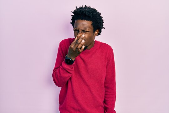 Young african american man wearing casual clothes smelling something stinky and disgusting, intolerable smell, holding breath with fingers on nose. bad smell