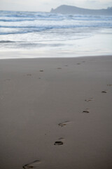 Footsteps on sandy beach and stormy sea waves at winter