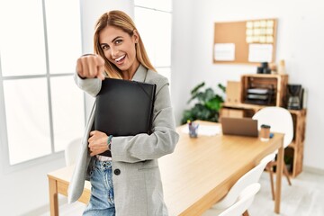 Blonde business woman at the office pointing to you and the camera with fingers, smiling positive and cheerful