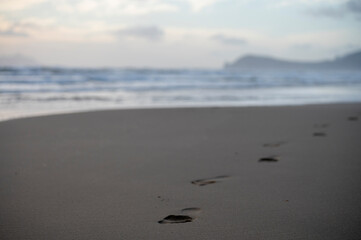 Footsteps on sandy beach and stormy sea waves at winter