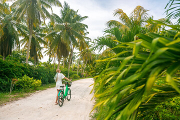 A girl walks near a old vintage bicycle on a tropical environment in the Seychelles. It is surrounded by palm trees. Copy space