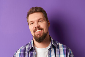 Happy bearded man in shirt smiling looking at camera on purple background. Young handsome stylish guy