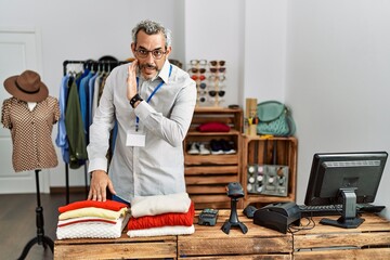 Middle age hispanic man working as manager at retail boutique hand on mouth telling secret rumor, whispering malicious talk conversation