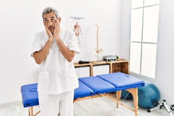 Middle age hispanic therapist man working at pain recovery clinic tired hands covering face, depression and sadness, upset and irritated for problem