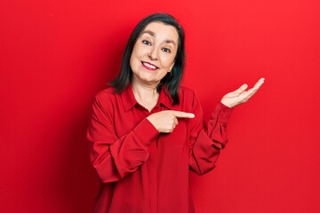 Middle age hispanic woman wearing casual clothes amazed and smiling to the camera while presenting with hand and pointing with finger.