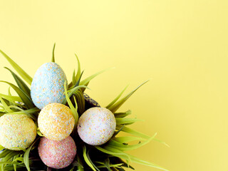 Top of view to the multicolored eggs bouquet with grass on yellow background. Copy space.