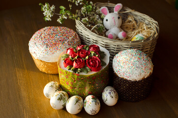 Easter composition cakes, kulich, pastry, festive decorated eggs, white knitted toy bunny on wooden table in basket, soft light, day light