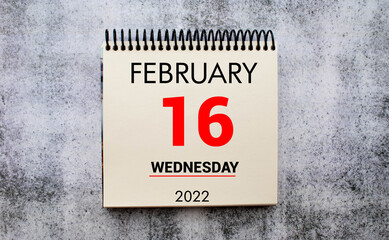 february 16. 16th day of month, calendar date. Stand for desktop calendar on beige wooden background.
