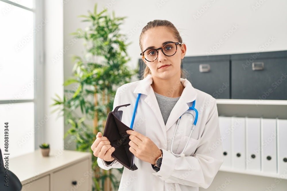 Poster Young blonde woman wearing doctor uniform showing empty wallet at clinic