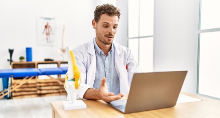 Young hispanic man wearing physiotherapist uniform having video call working at clinic