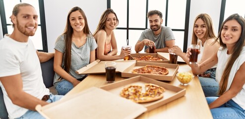 Group of young people smiling happy eating italian pizza sitting on the table at home