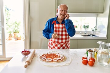 Senior man with grey hair cooking pizza at home kitchen looking stressed and nervous with hands on mouth biting nails. anxiety problem.
