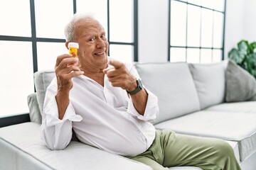 Senior man holding pills pointing fingers to camera with happy and funny face. good energy and vibes.