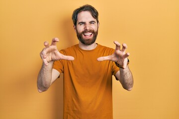 Caucasian man with beard wearing casual yellow t shirt smiling funny doing claw gesture as cat,...