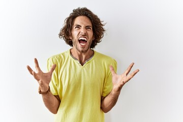 Young hispanic man standing over isolated background crazy and mad shouting and yelling with...