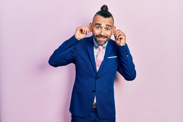 Young hispanic man wearing business suit and tie smiling pulling ears with fingers, funny gesture. audition problem