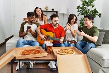 Group of young friends having party eating italian pizza and playing classical guitar at home.
